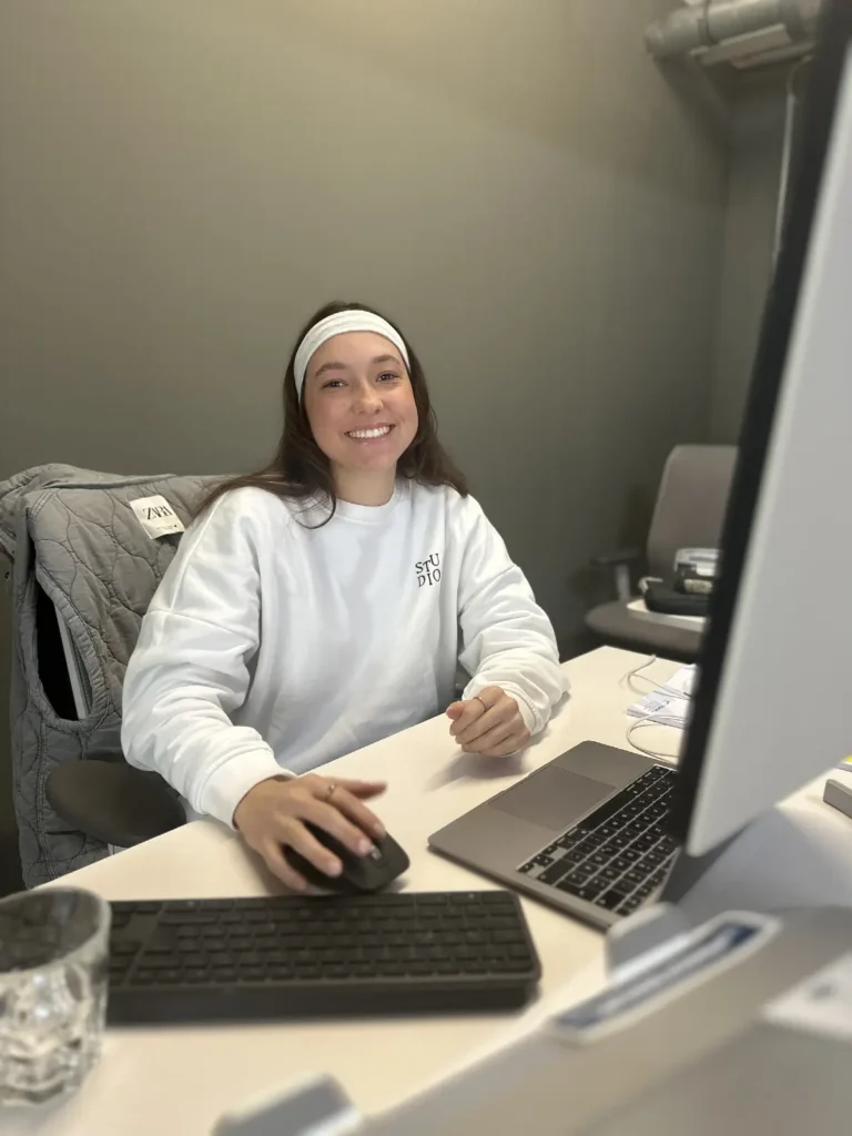 Mitarbeiterin aus dem Ministerium sitzt vor einem Bildschirm und schaut motiviert in die Kamera