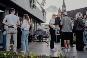 Menschen treffen sich bei einem Event im Freien mit Blick auf Gebäude.